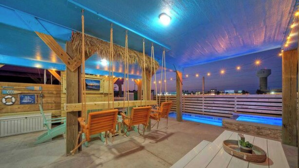 An outdoor seating area with wooden benches and a thatched roof structure, overlooking a body of water. - Totally Beachin by Avantstay Private Heated Pool, Hot Tub + Fire Pit! (Port Aransas)