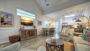 A spacious living room with a large TV, comfortable seating, a dining area, and a kitchen in the background. - 2 Blocks to the Beach, Patio, Resort Pool w/ Slide Tranquil Tides by Avantstay (Port Aransas)