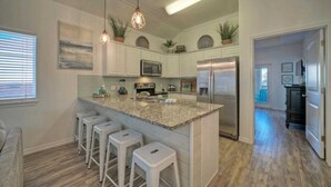 A modern kitchen with white cabinets, a granite countertop, stainless steel appliances, and bar stools. - Isla View by Avantstay Resort Pool, Near Beach (Port Aransas)