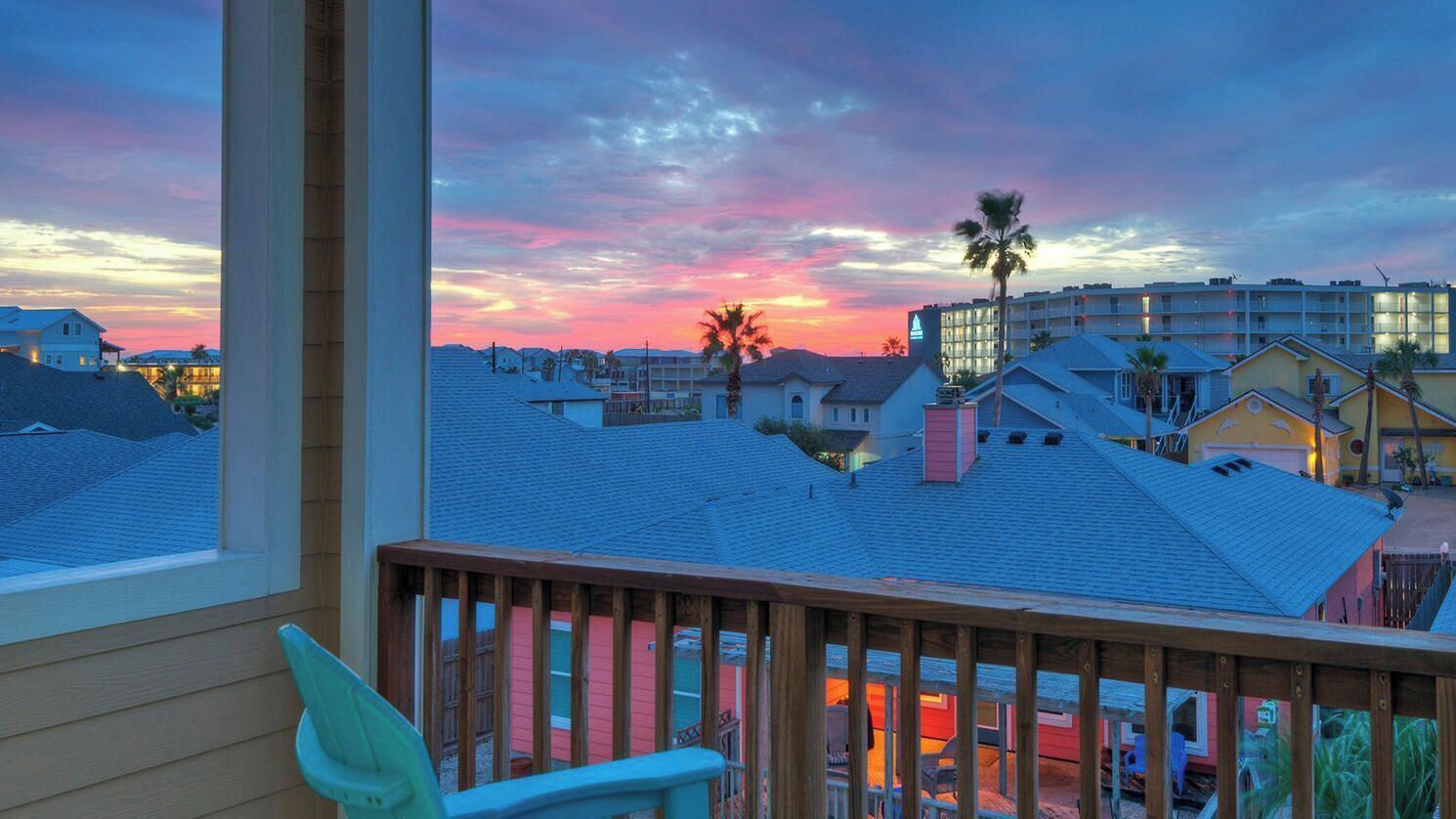 A view from a balcony with a wooden railing, overlooking a residential area with houses and a hotel.