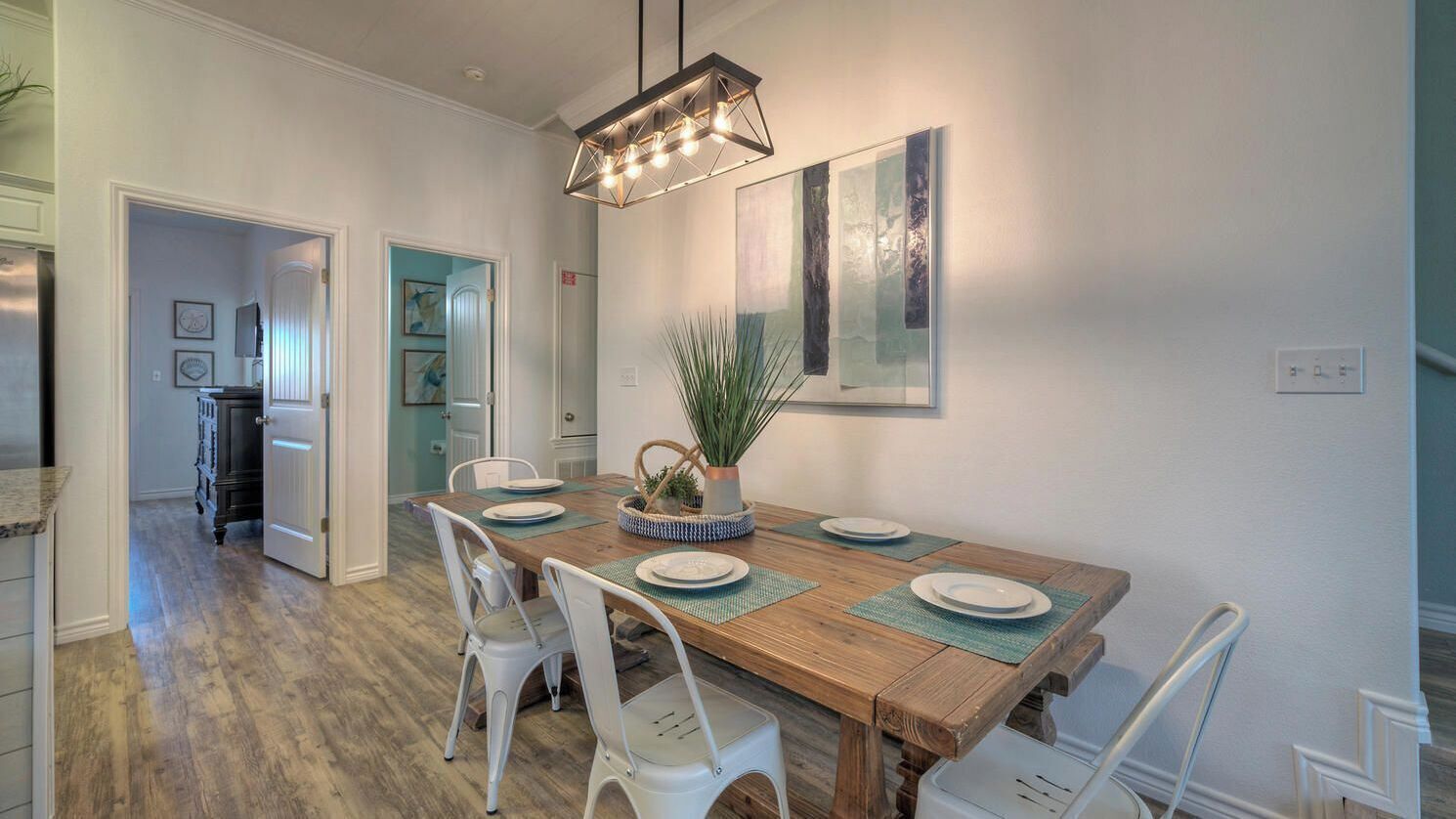 Un coin repas avec une table en bois, des chaises blanches, un luminaire suspendu et une plante en pot.