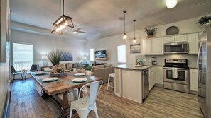 Une cuisine spacieuse avec un coin repas, un plancher en bois, des meubles blancs et des appareils électroménagers modernes.