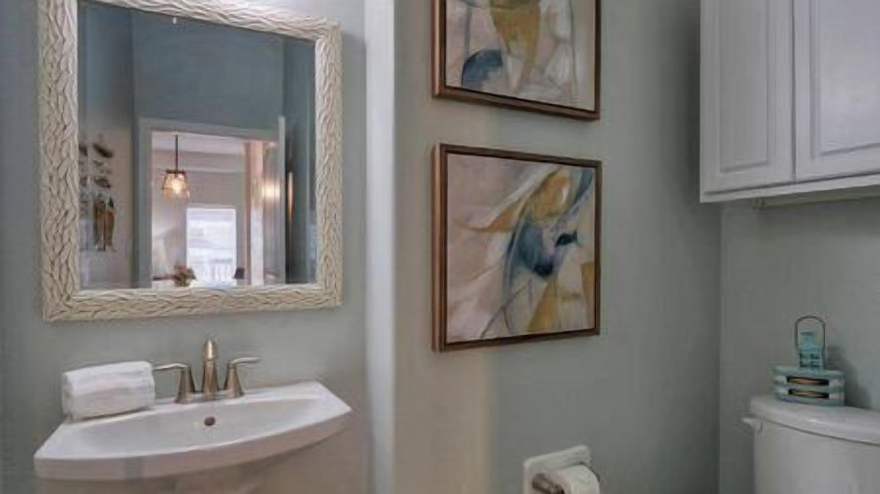 A bathroom with a white sink, a mirror with a textured frame, and two abstract paintings on the wall.