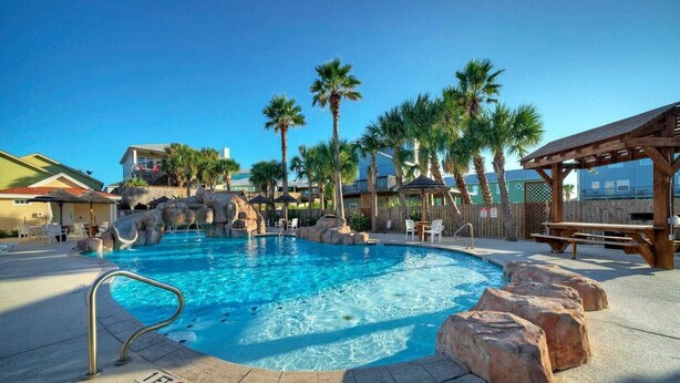 A pool with a wooden deck, palm trees, and a wooden pergola. - Isla View by Avantstay Resort Pool, Near Beach (Port Aransas)
