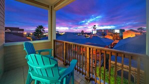 A balcony with two chairs and a view of a residential area during twilight. - Isla View by Avantstay Resort Pool, Near Beach (Port Aransas)