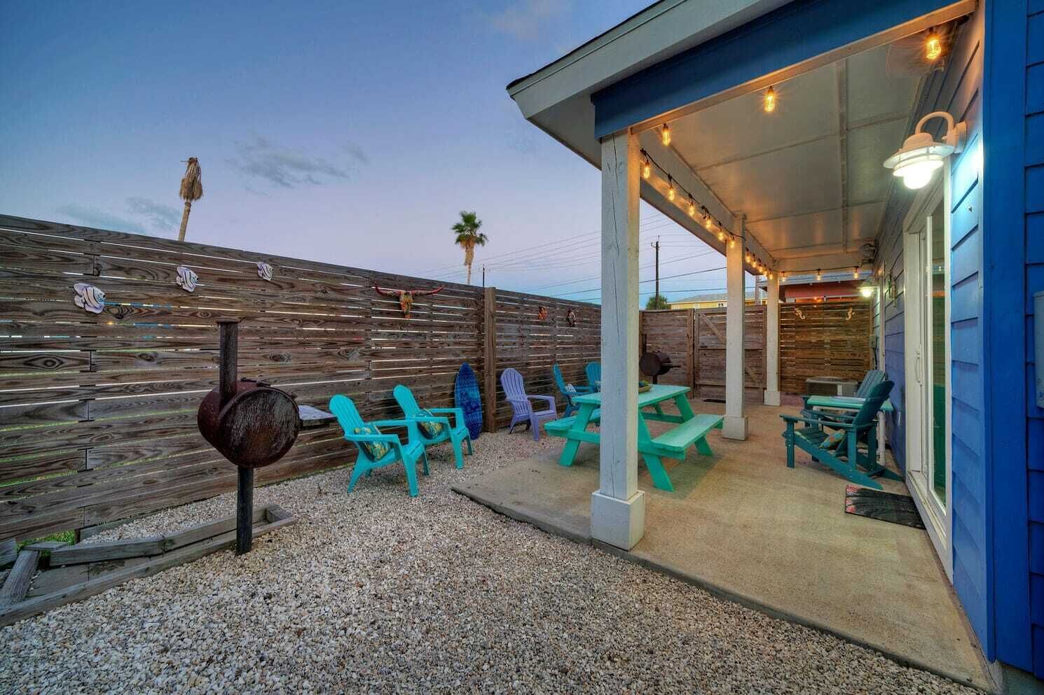 An outdoor patio area with turquoise chairs, a barbecue grill, and a covered seating area with string lights.