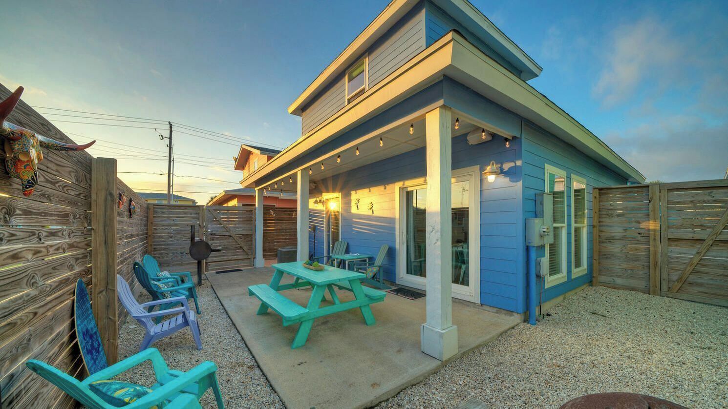 A two-story building with a covered patio area, outdoor seating, and a wooden fence.
