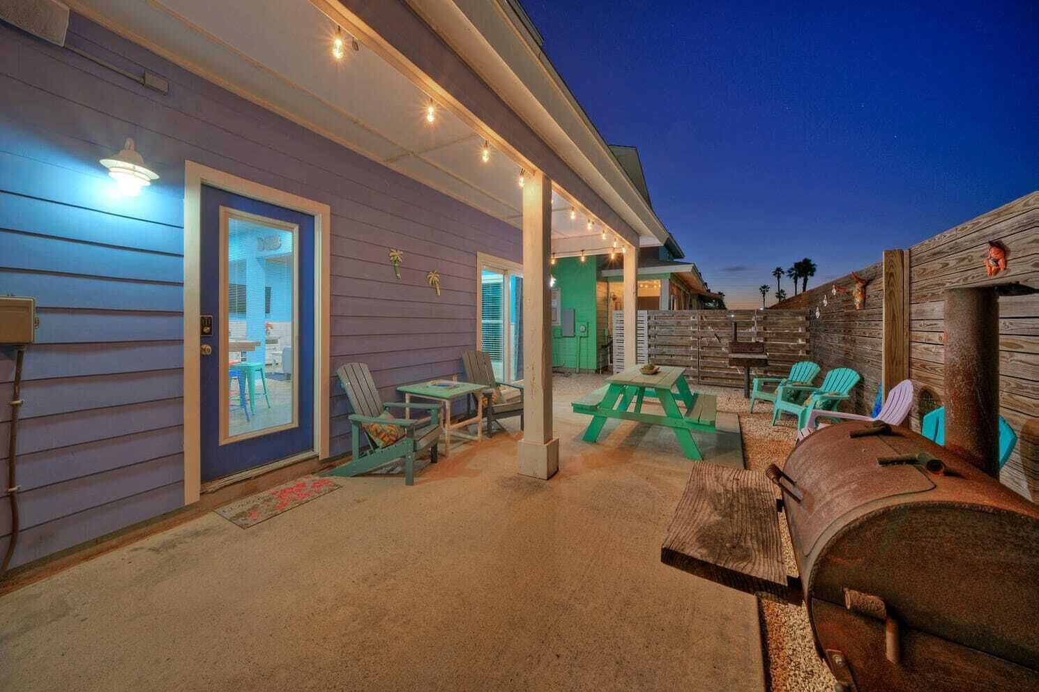 Une terrasse extérieure avec des fauteuils Adirondack verts, une table de pique-nique et un tonneau en bois.
