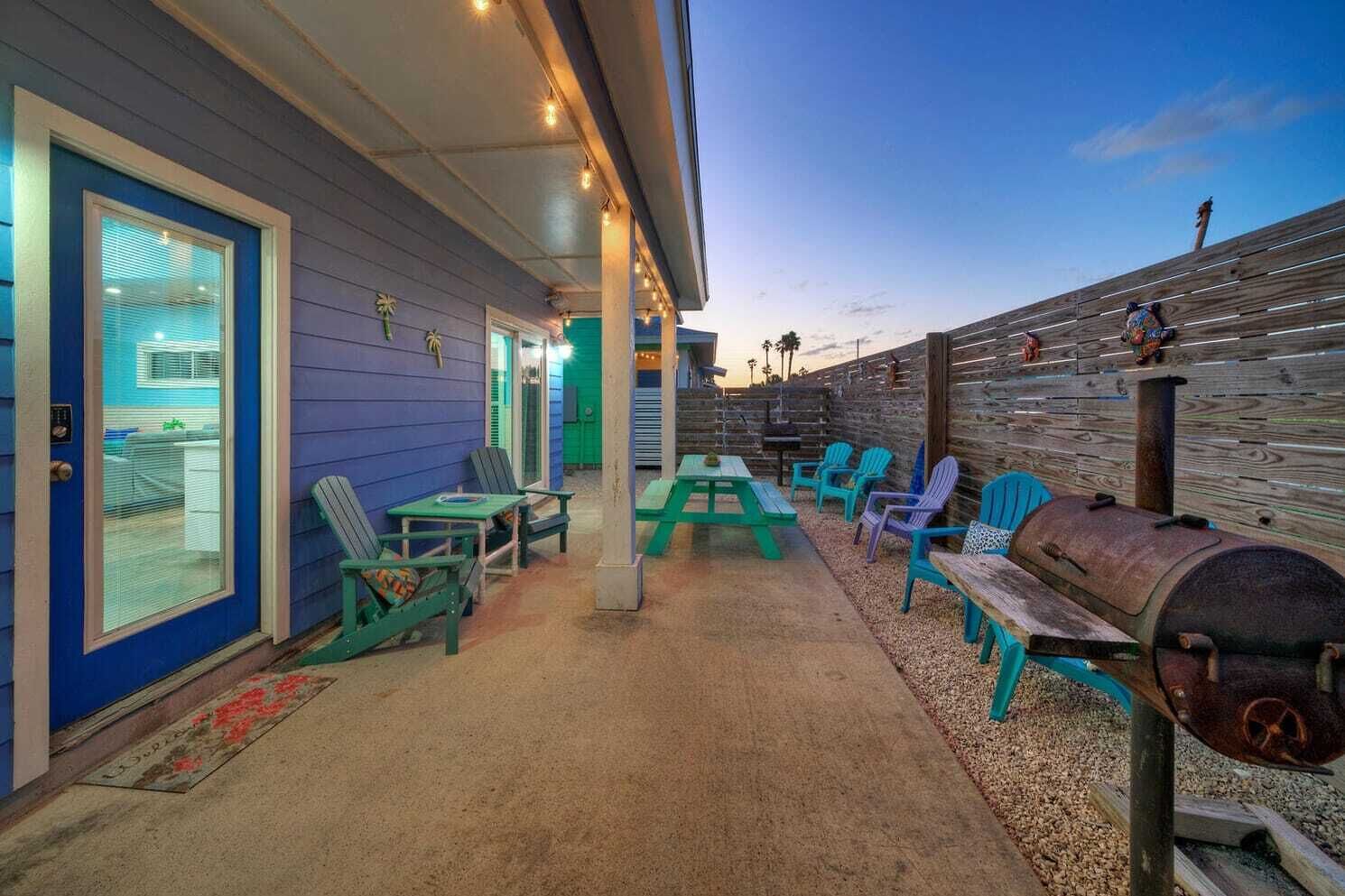 A covered outdoor area with blue walls, a grill, and green chairs.