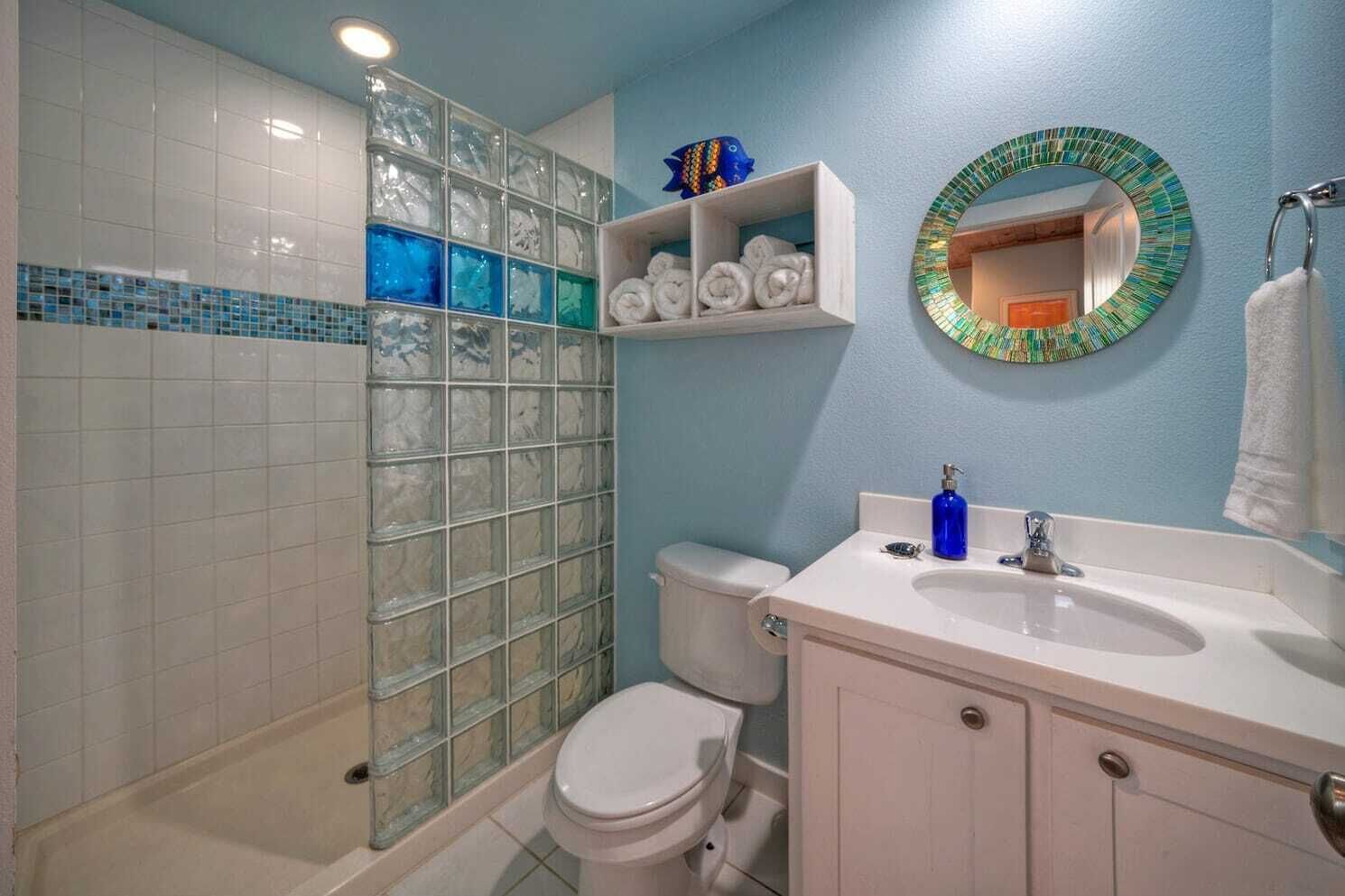 Une salle de bain avec une douche à parois de verre, des toilettes, un lavabo avec un miroir et une étagère avec des serviettes.