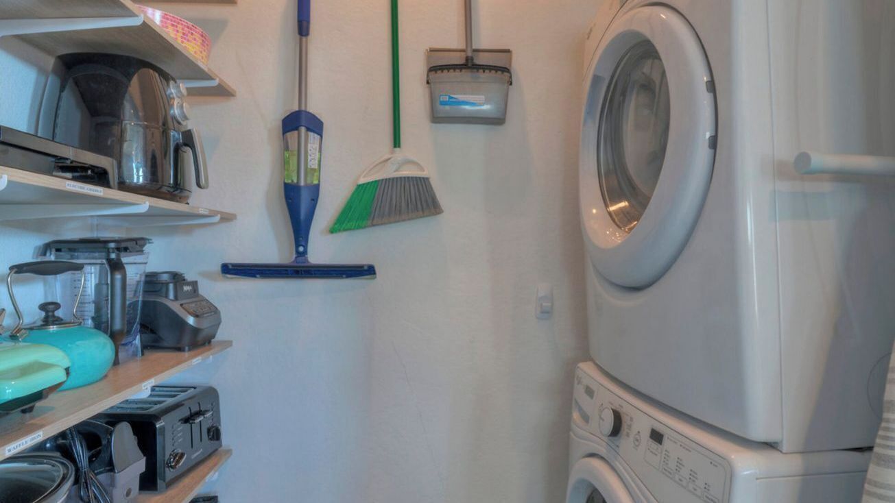 A laundry room with a washing machine, a broom, and various appliances on shelves.