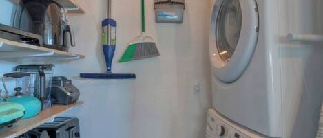 A laundry room with a washing machine, a broom, and various appliances on shelves.