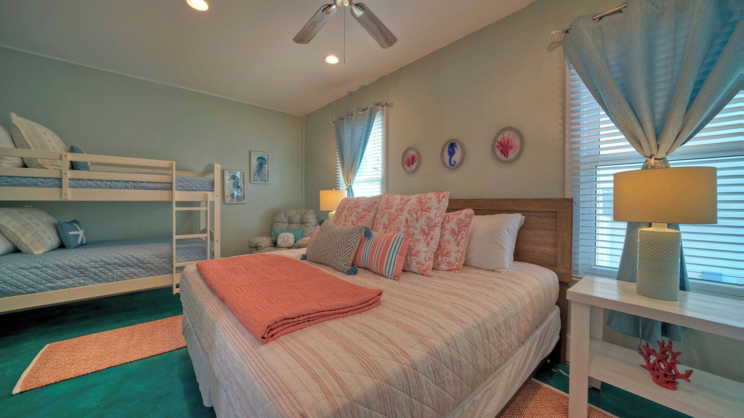A bedroom with bunk beds, a large bed with multiple pillows, a ceiling fan, and a nightstand with a lamp.