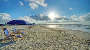 En strand med parasoller, solstolar och en brygga som sträcker sig ut i vattnet.