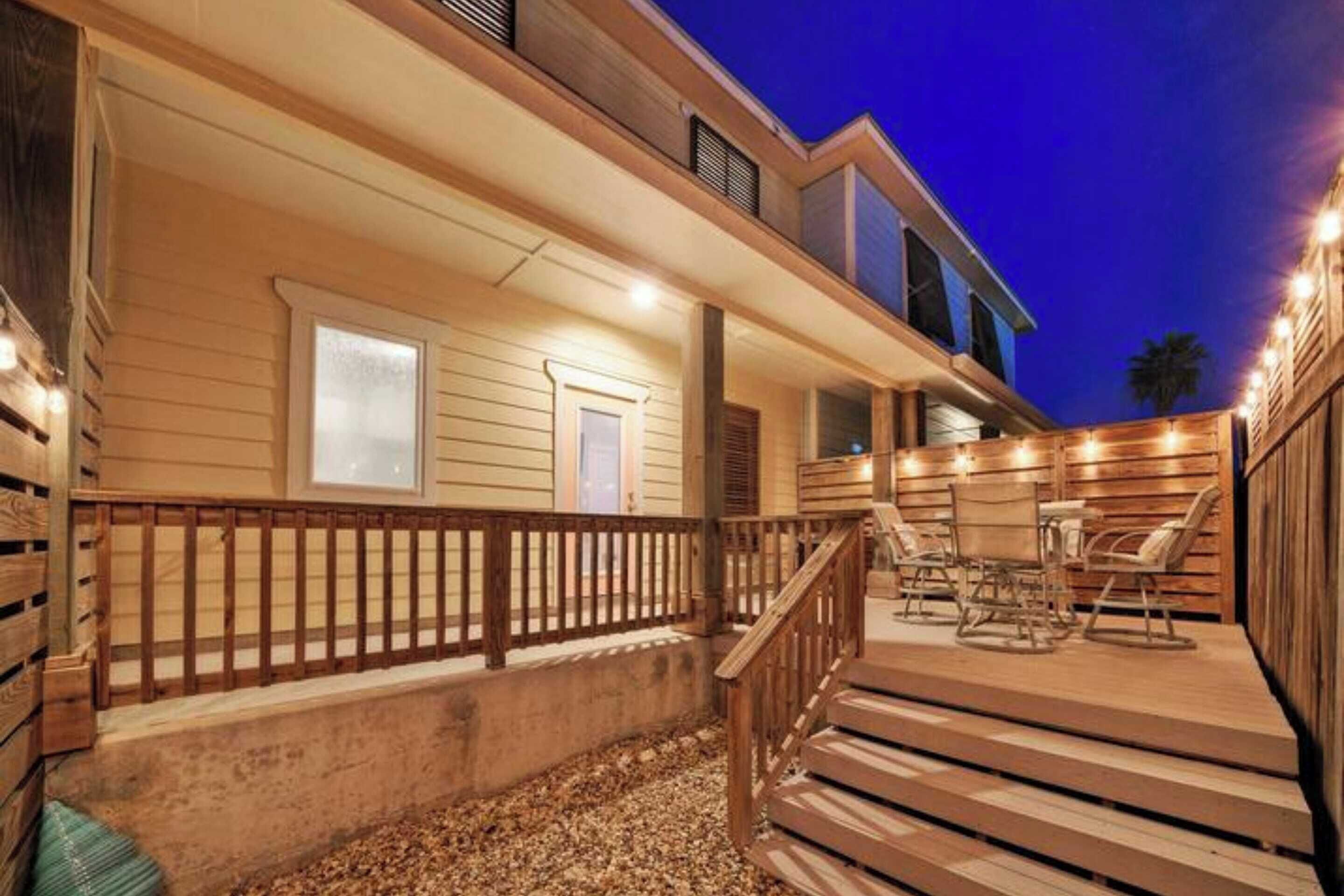 A wooden deck with outdoor seating, a staircase, and a building with a porch.