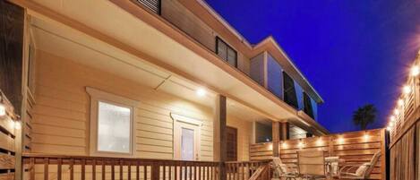 A wooden deck with outdoor seating, a staircase, and a building with a porch.