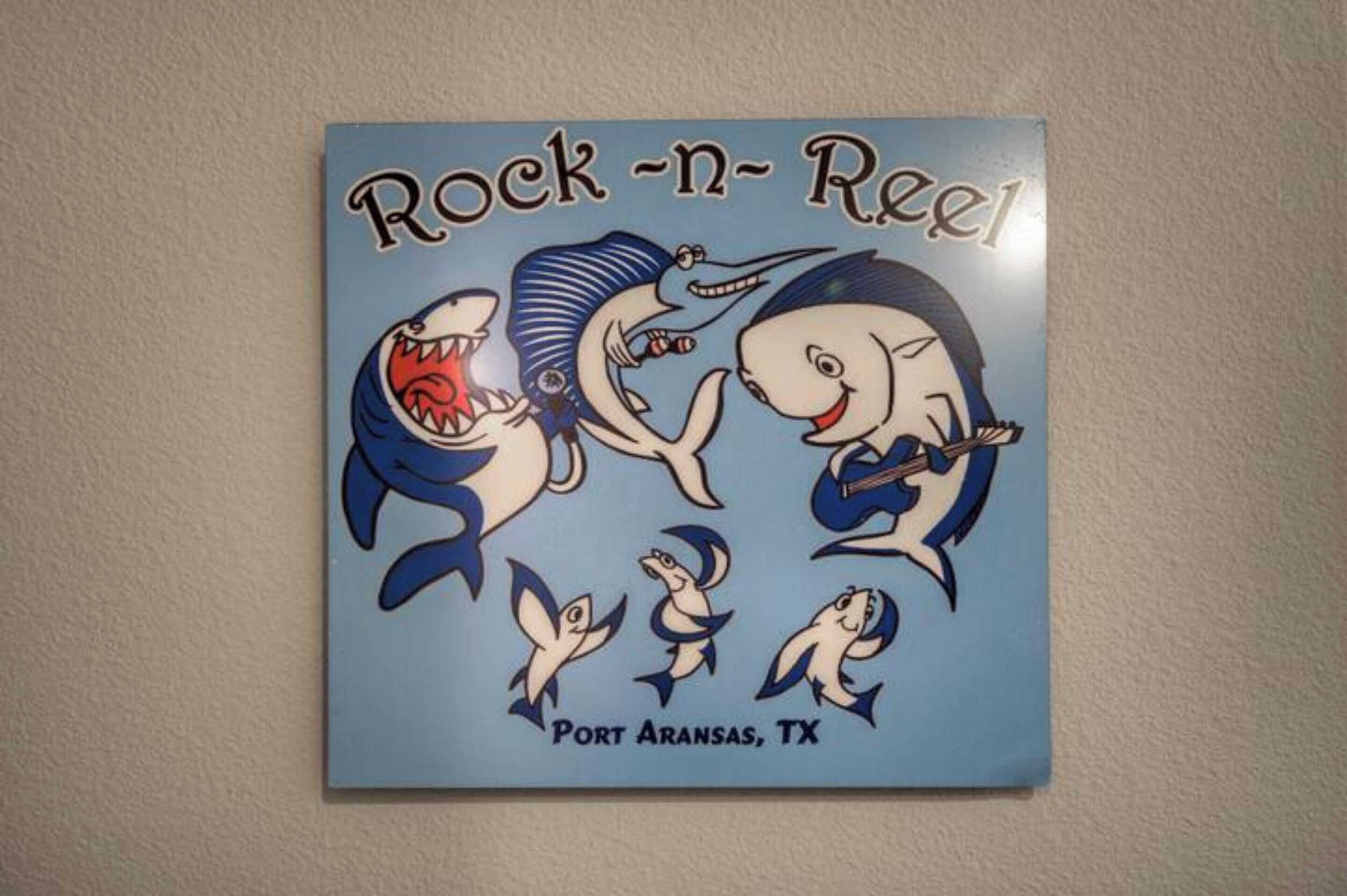 Un autocollant mural représentant des requins de dessin animé, avec les inscriptions « Rock 'n' Reel » et « Port Aransas, TX ».