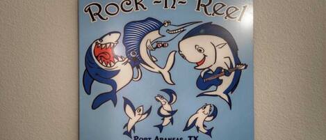 Un autocollant mural représentant des requins de dessin animé, avec les inscriptions « Rock 'n' Reel » et « Port Aransas, TX ».