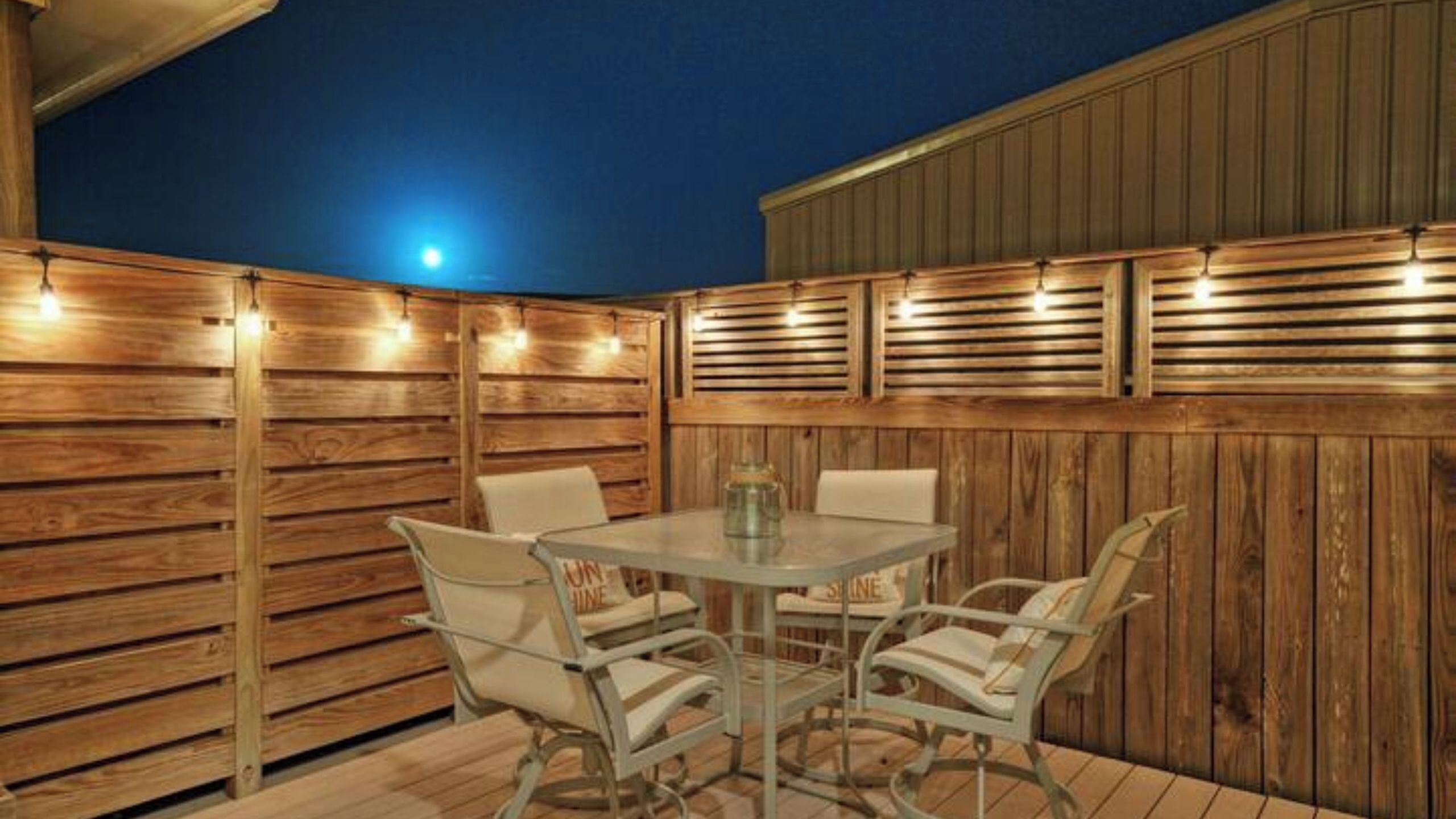 An outdoor patio with a table and chairs, wooden walls, and string lights.