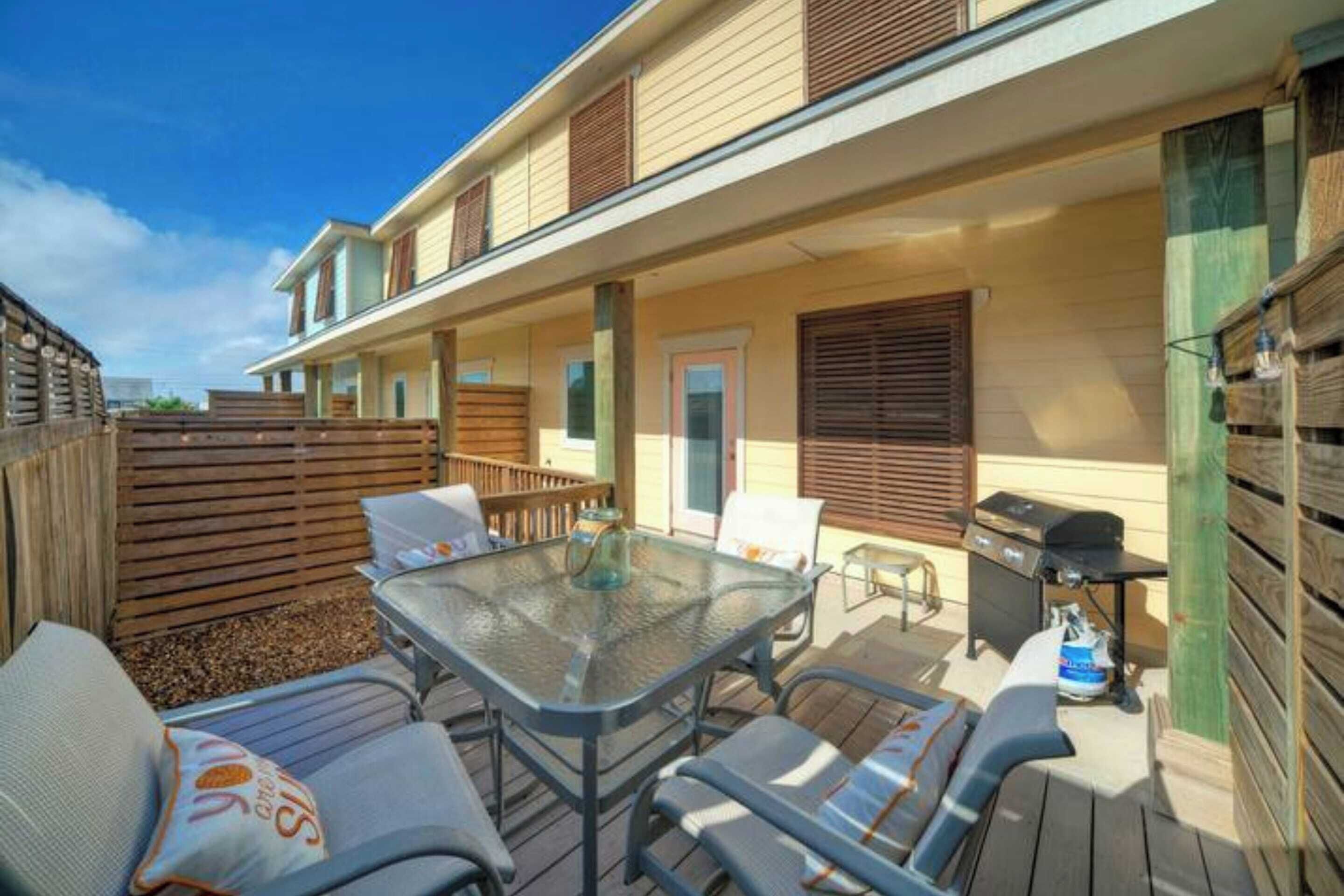 Un patio techado al aire libre con una mesa de vidrio, sillas y una parrilla.