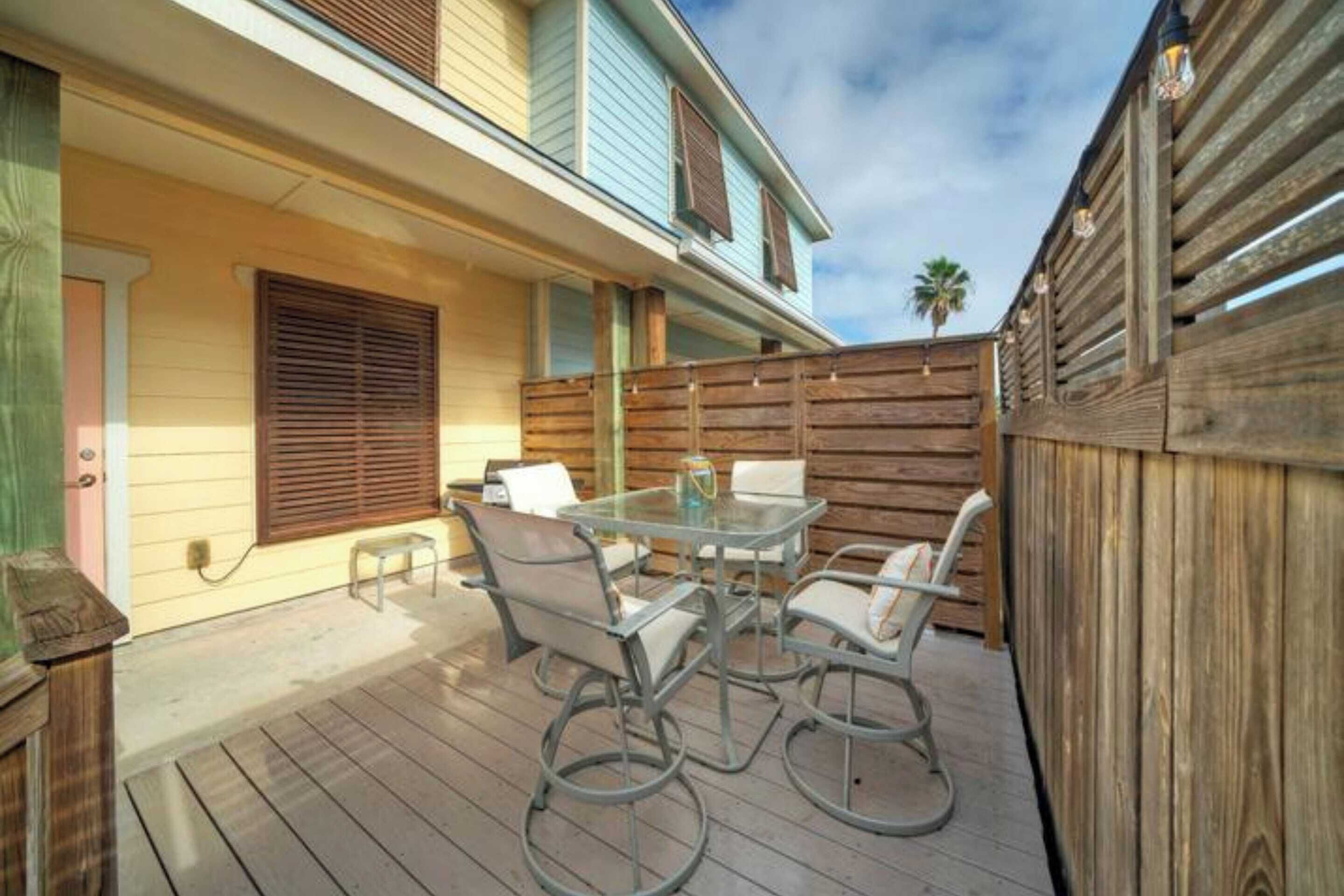 Une terrasse avec une table et des chaises en verre, une clôture en bois et un bâtiment à la façade bleu clair.