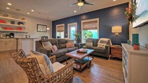 A modern living room with a dark blue accent wall, a ceiling fan, and a wooden coffee table. - Pool, Walk to Old Town + Eateries, Nightlife, Shopping Rock N Reelby Avantstay (Port Aransas)
