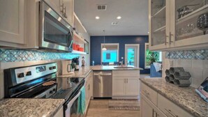 A modern kitchen with stainless steel appliances, white cabinetry, and a blue accent wall. - Pool, Walk to Old Town + Eateries, Nightlife, Shopping Rock N Reelby Avantstay (Port Aransas)