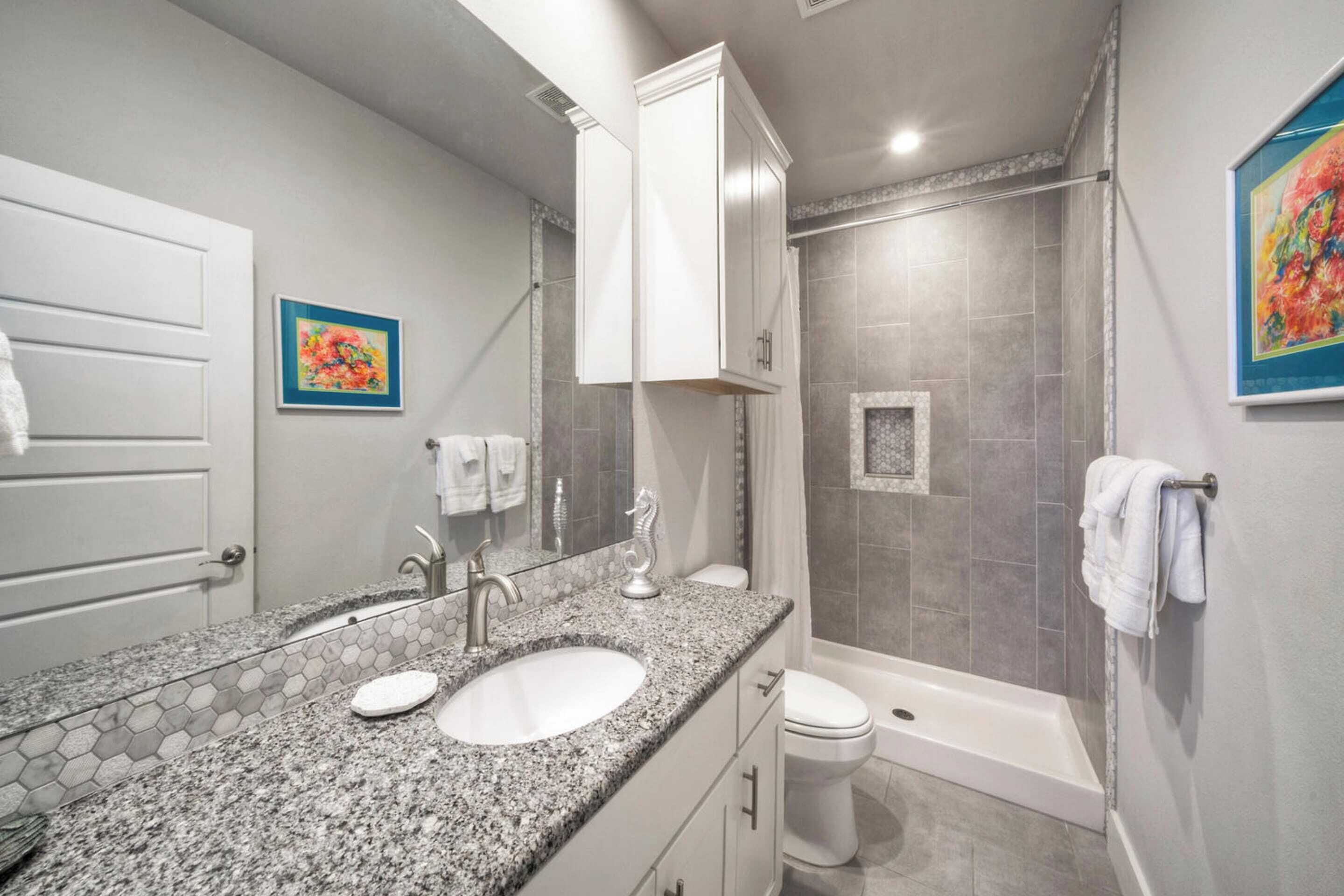 A bathroom with a granite countertop sink, a toilet, and a shower area.