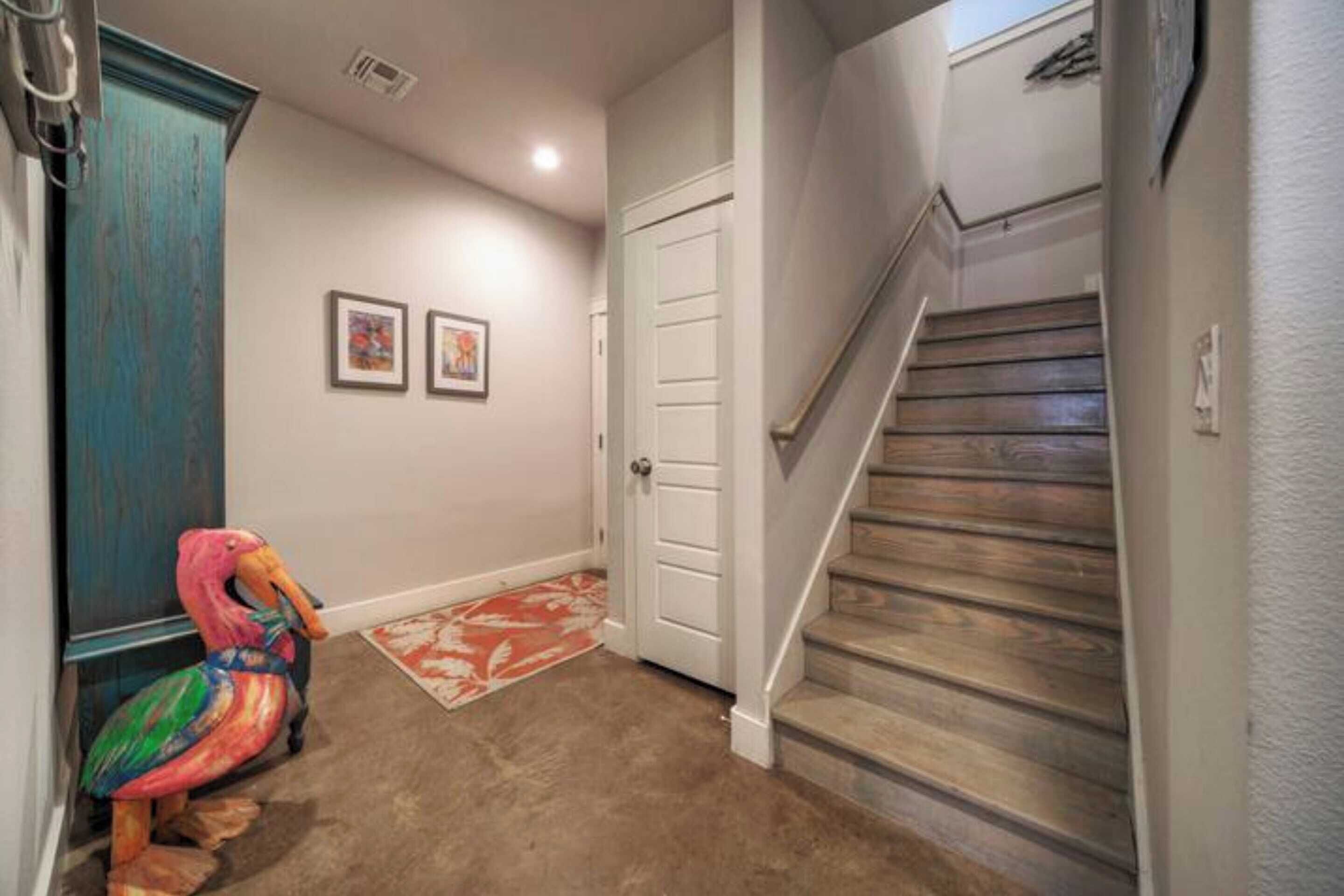 Un pasillo con una escalera de madera, una puerta y una decoración de flamenco colorido.
