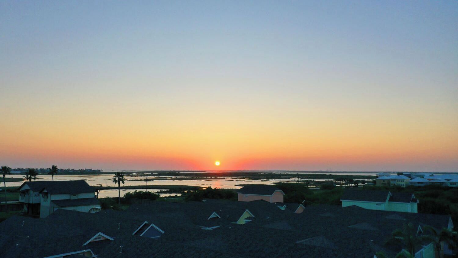A sunset over a residential area with houses and a body of water.