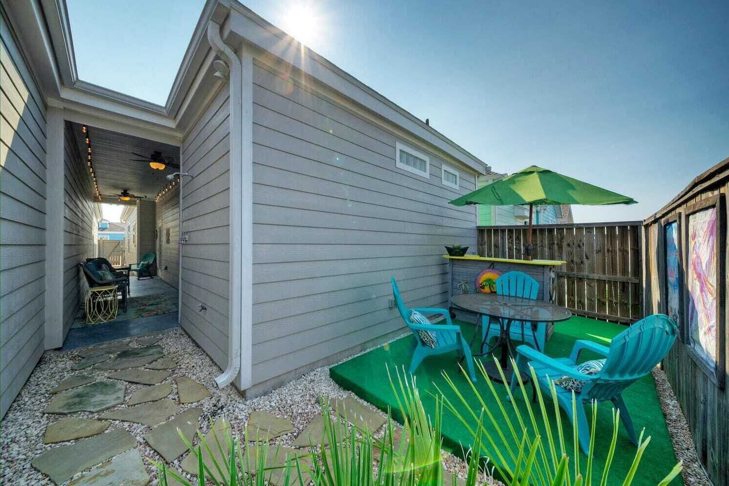 Une terrasse avec une table et des chaises, un parasol vert et une clôture en bois.