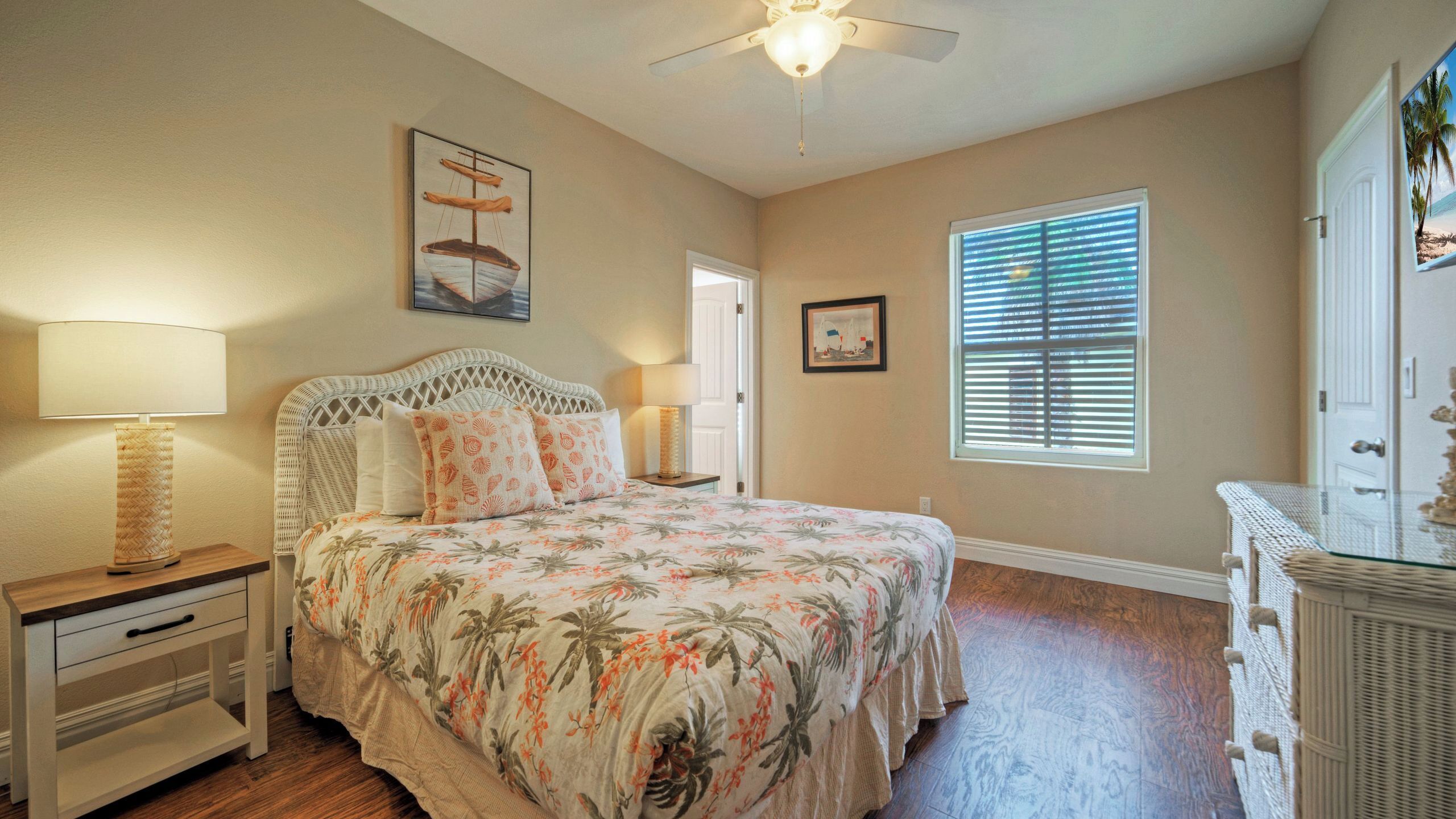 A bedroom with a bed, nightstands, a ceiling fan, a window with blinds, and a door.