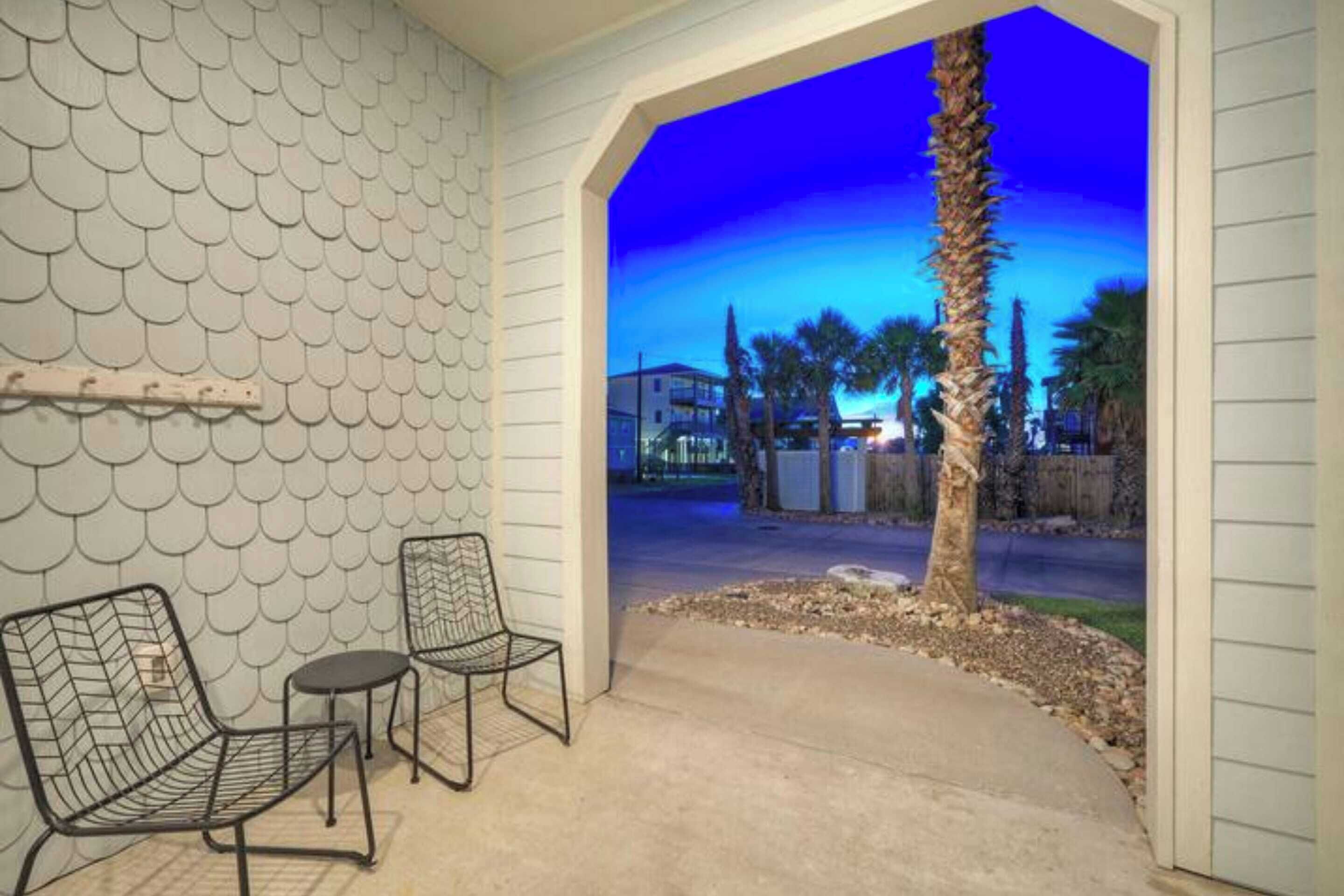 An outdoor patio area with two metal chairs, a small table, and a decorative wall with a scalloped pattern.