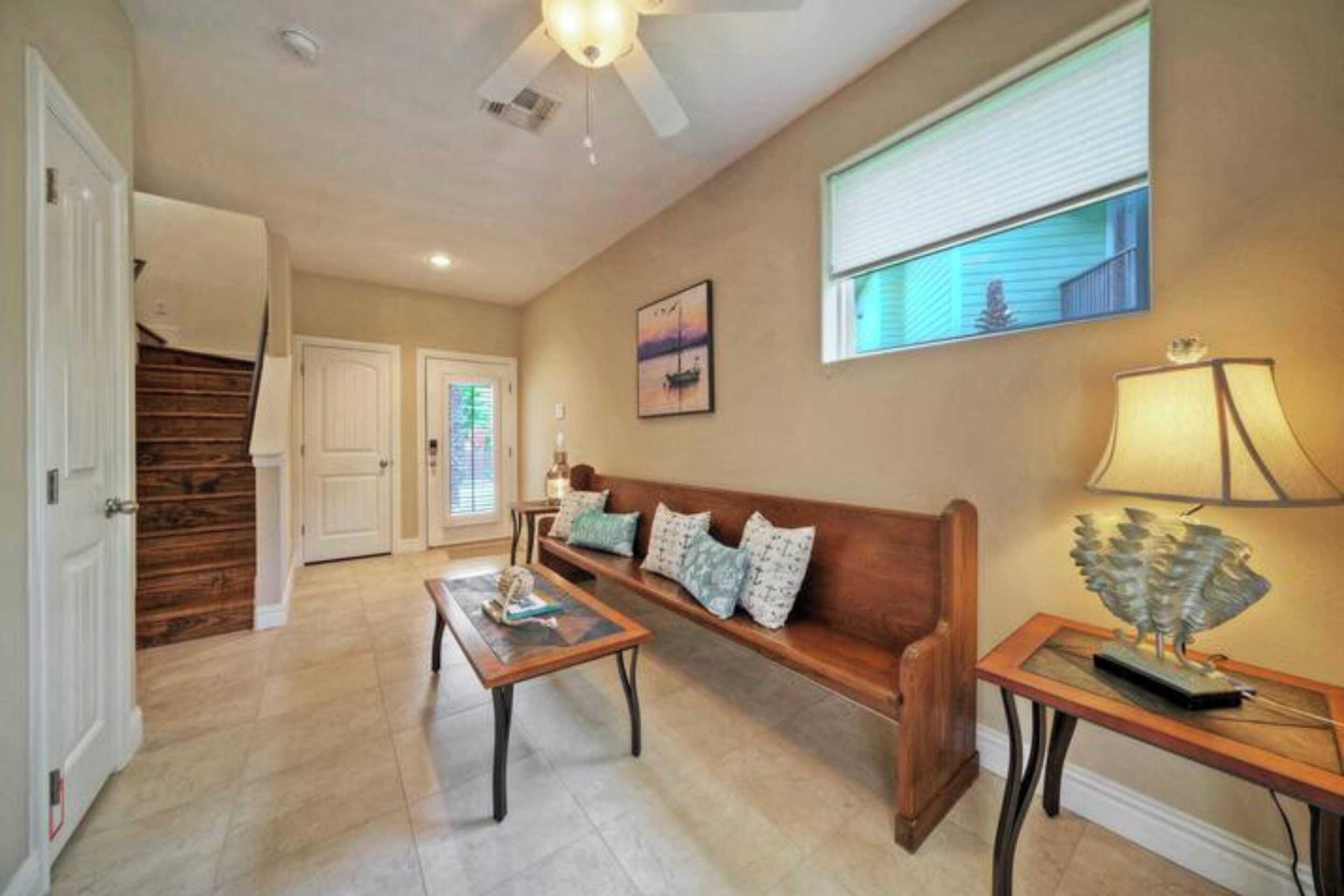 A spacious living room with a wooden bench, a coffee table, and a lamp. There is a staircase leading to another room.