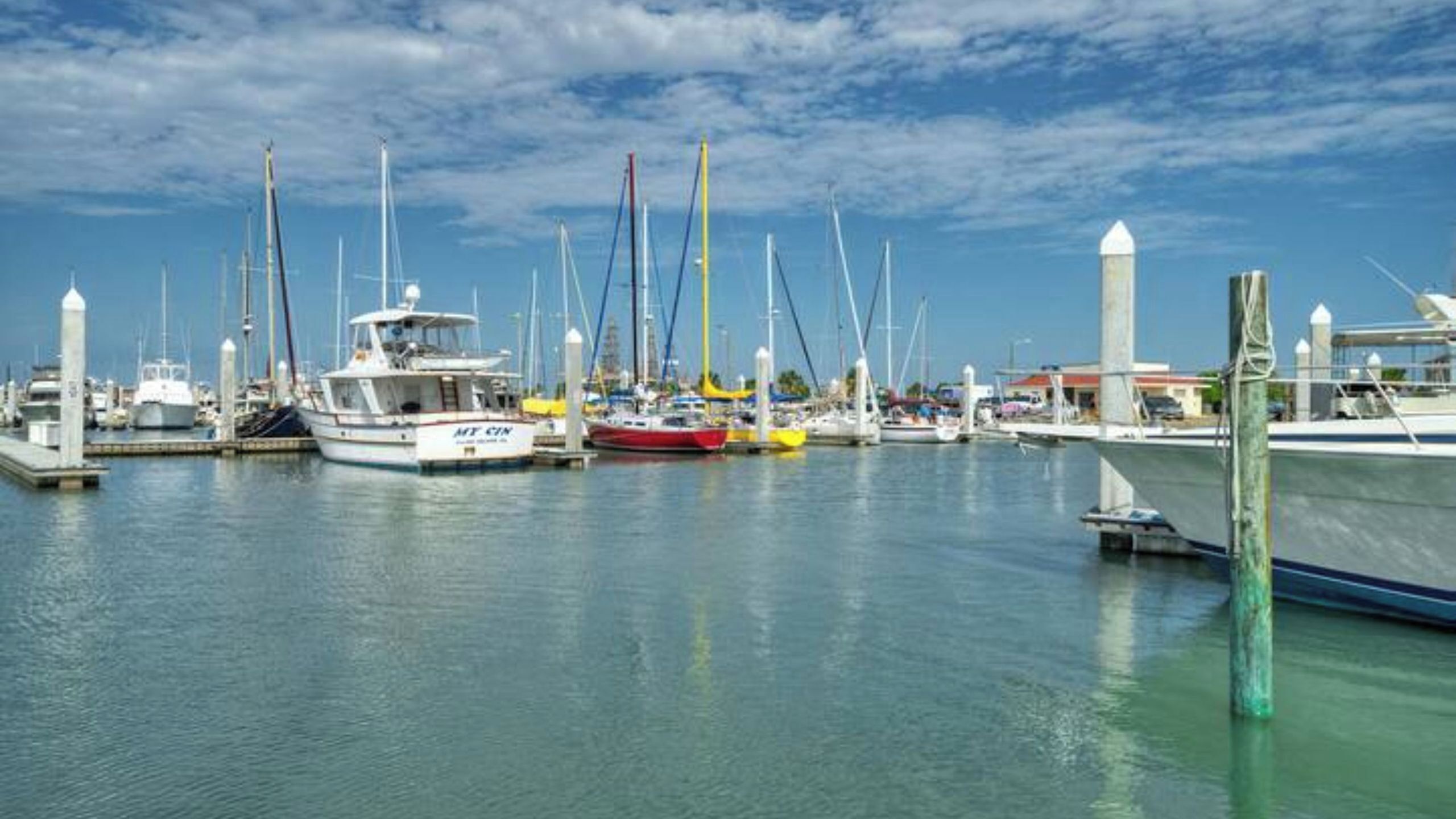 A marina with multiple boats docked, a clear sky, and calm water.