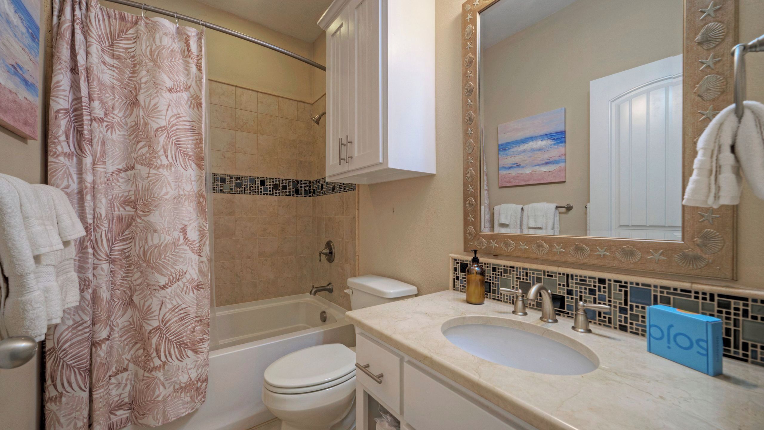 A bathroom with a shower curtain, toilet, sink, and a large mirror with a decorative frame.