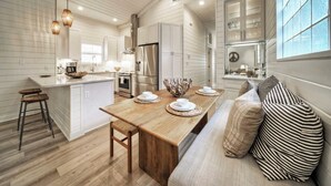 Une cuisine moderne avec des meubles blancs, un îlot central en bois et un coin repas comprenant un banc et des coussins à rayures.