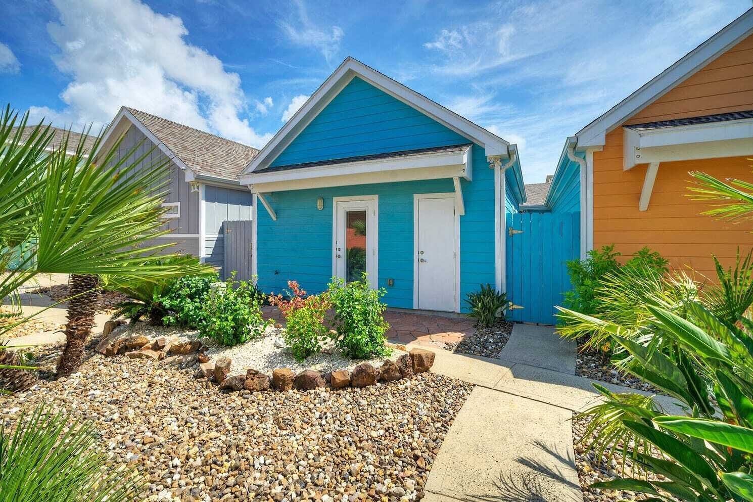 A residential property with a blue house, a front door, and a small garden with rocks and plants.