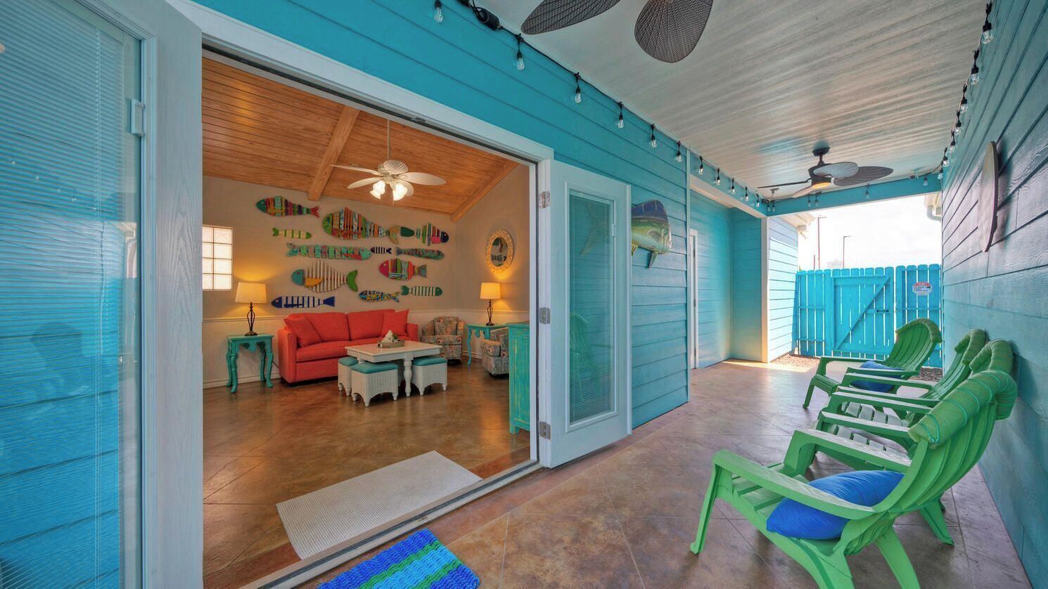 A covered outdoor area with a ceiling fan, a pool, and a seating area with green chairs.
