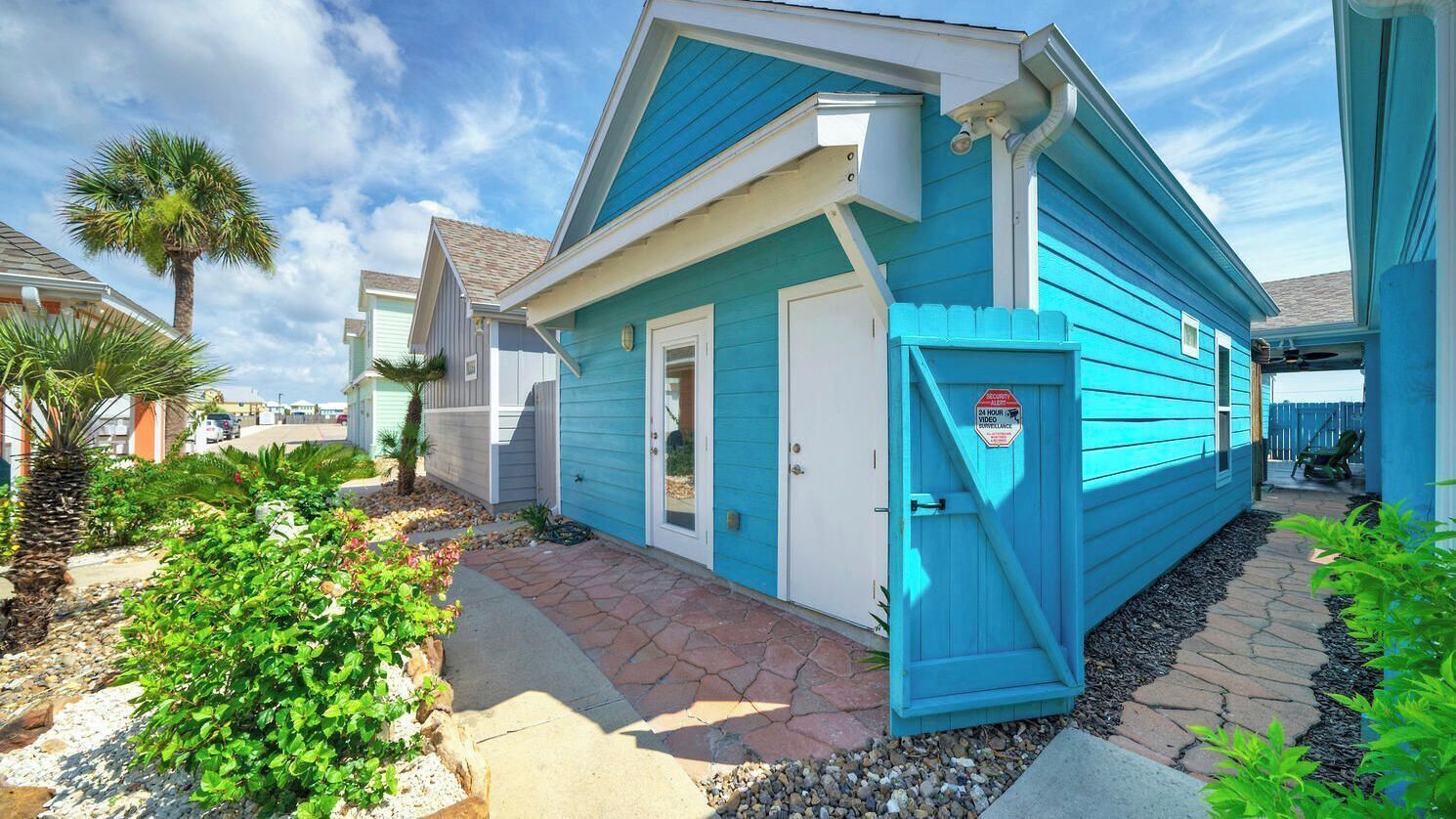 A blue house with a gated entrance, a small porch, and a stone pathway leading to the door.