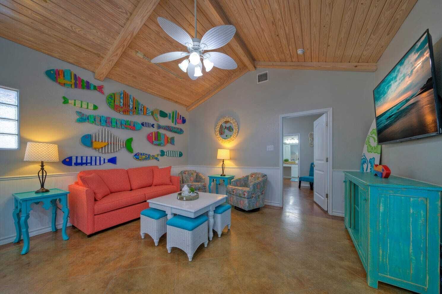 Un salon spacieux avec un plafond haut, un ventilateur de plafond, un canapé rouge, une table basse blanche et un meuble turquoise.