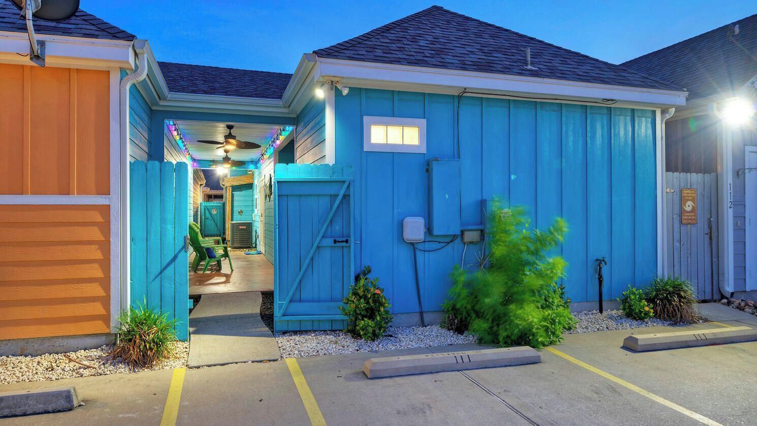 A building with a blue exterior, a door, and a small garden area with plants.