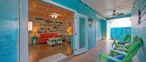 A spacious living area with a red sofa, green chairs, and a wooden ceiling fan.