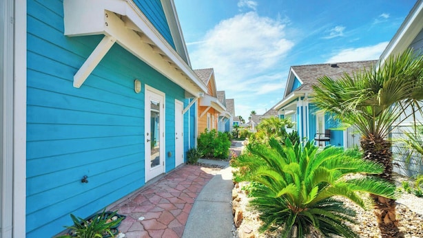 A row of blue houses with a pathway and palm trees. - Coastal Vibe by Avantstay Sunset at the Pool and Playscape (Port Aransas)