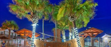 A sign with 'Pirates Bay' written on it, surrounded by palm trees and a fence.
