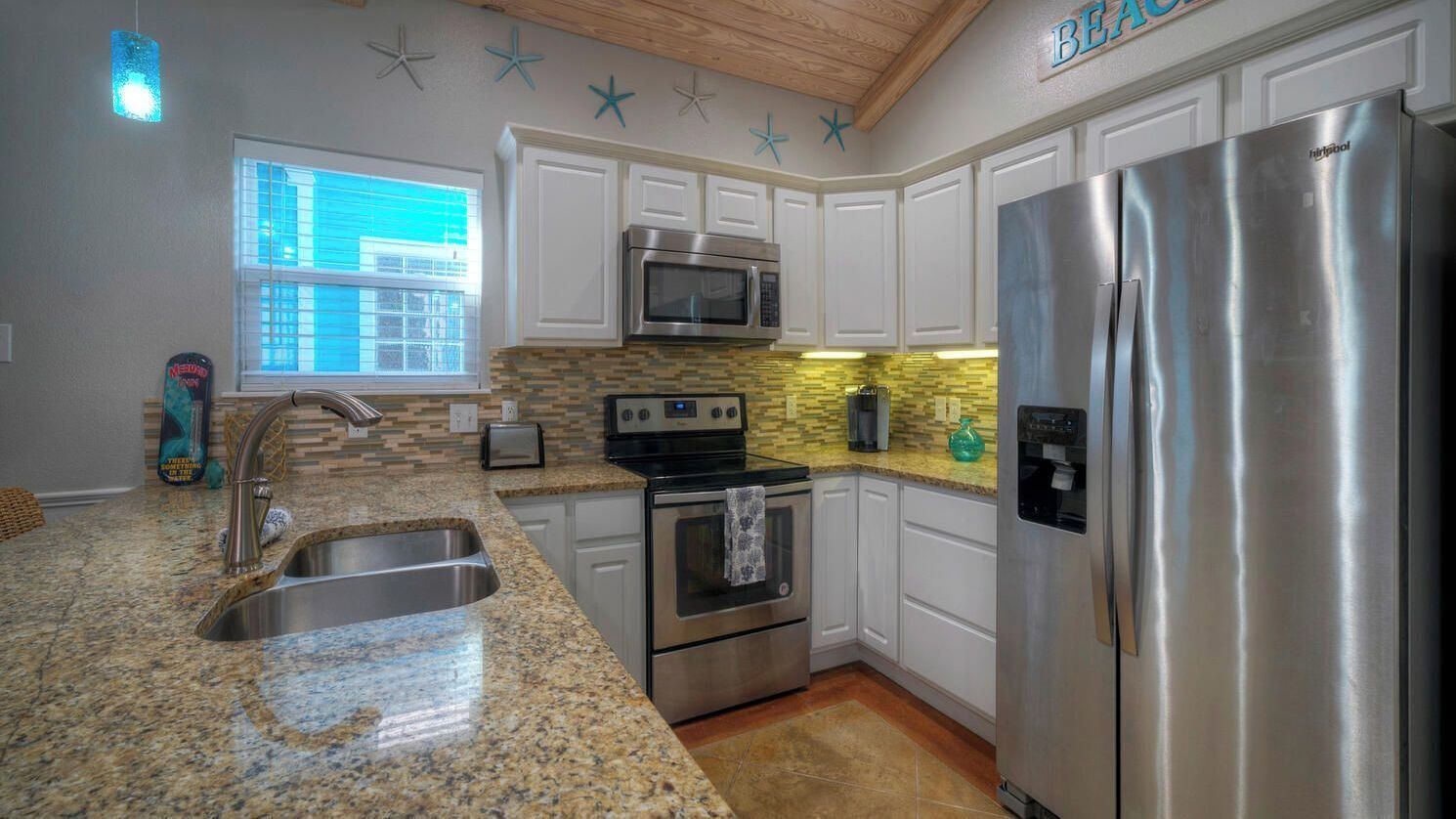 A kitchen with white cabinets, a stainless steel refrigerator, a microwave, and a stove.