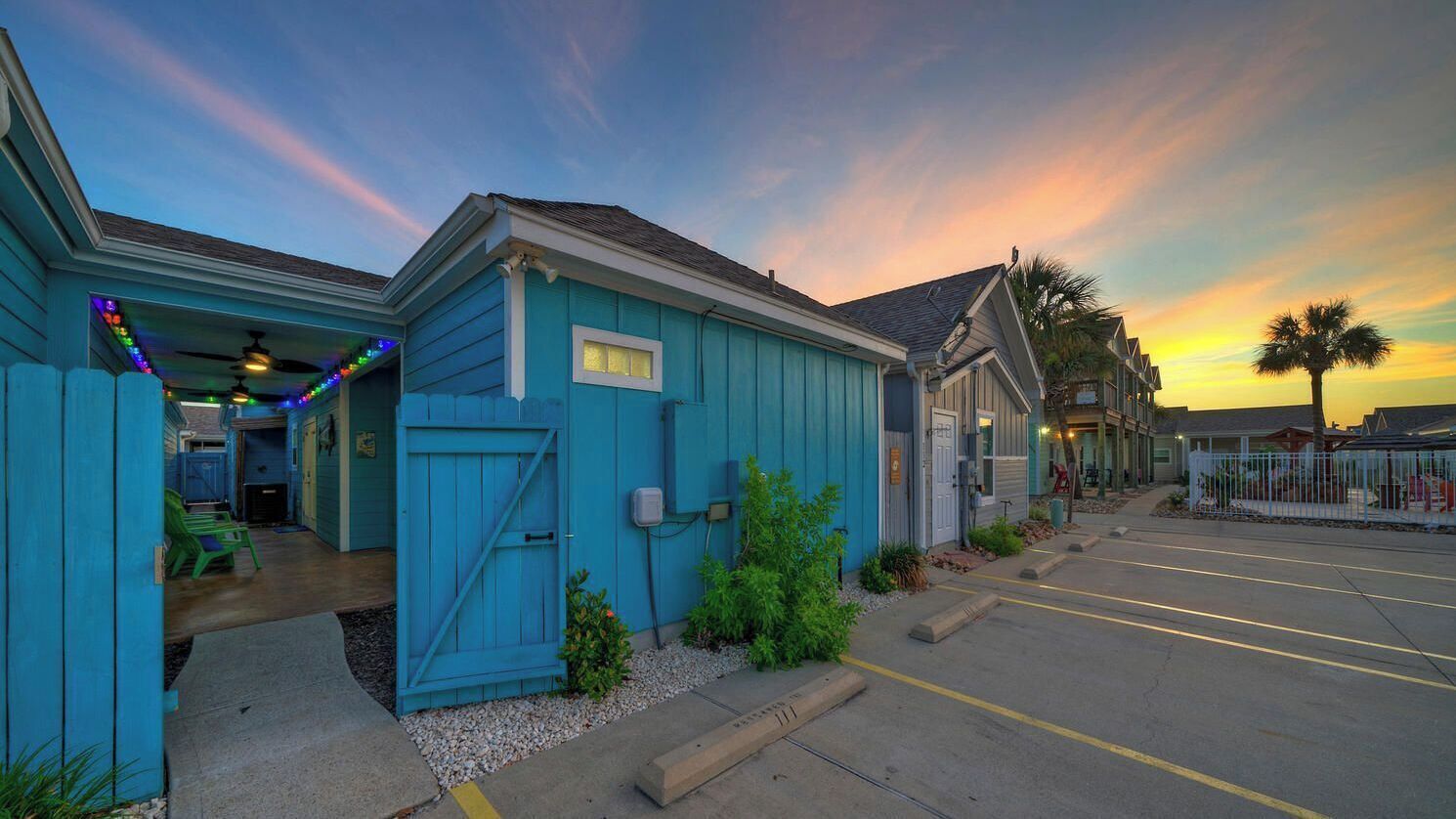 A blue building with a garage, a parking lot, and a sunset in the background.
