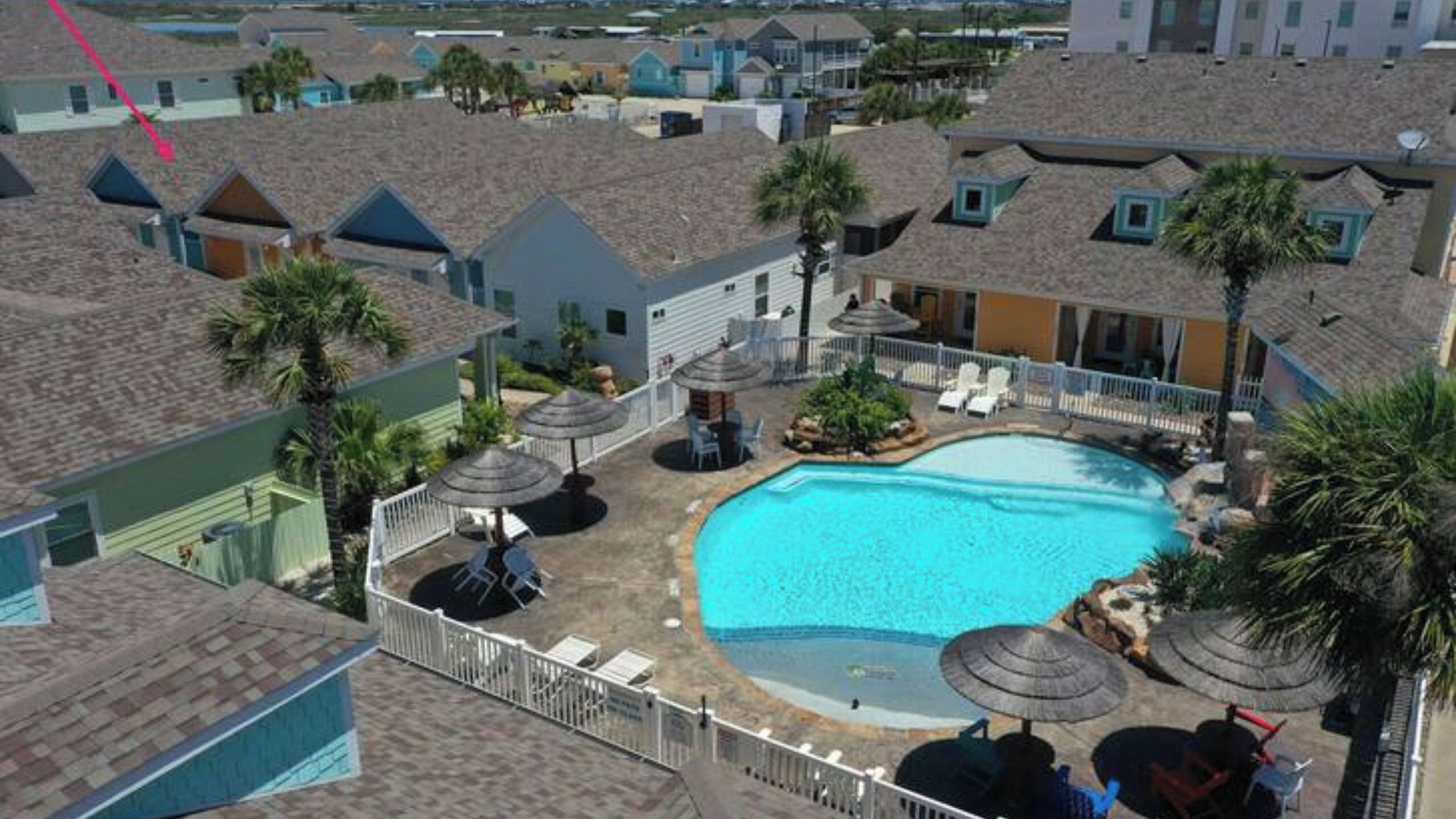 A residential area with a swimming pool surrounded by umbrellas and lounge chairs.
