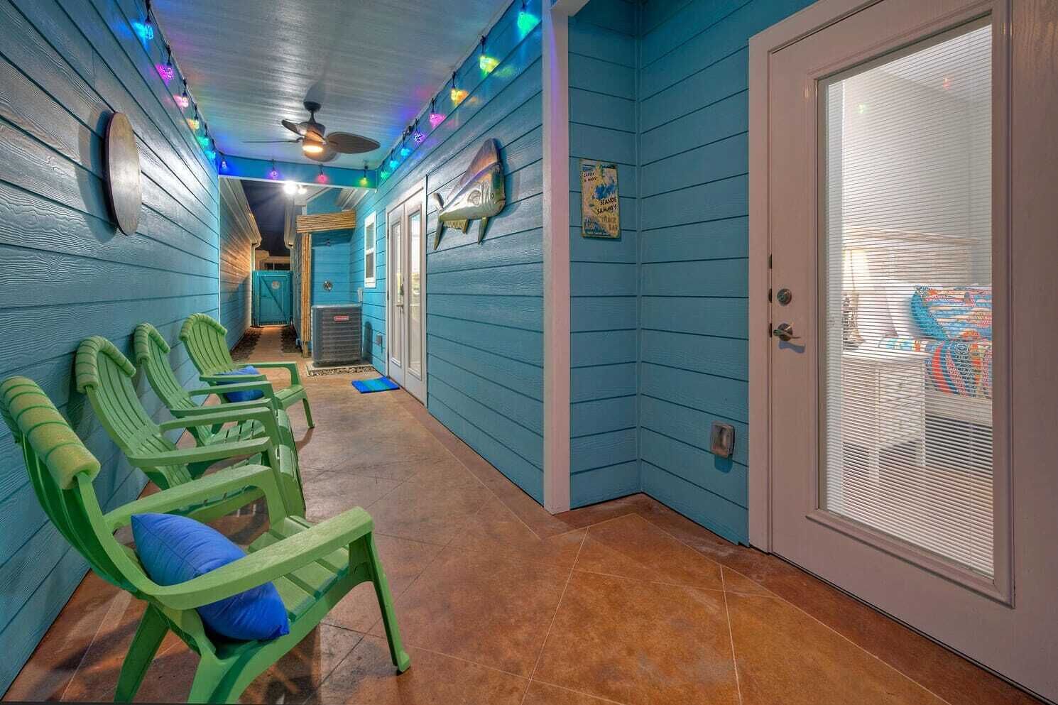 A hallway with teal walls, green chairs, a ceiling fan, and a door with a window.