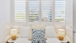 A bedroom with a bed, two bedside lamps, and three windows with blinds.